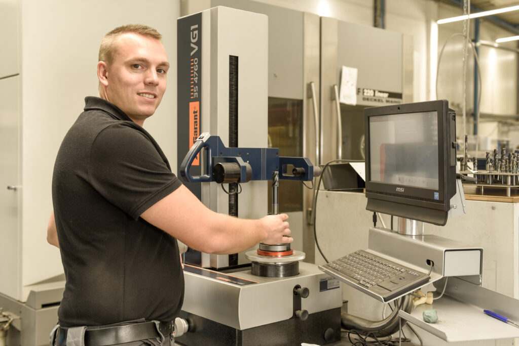 Lächelnder Mitarbeiter bedient Prüfmaschine für Bohrer in Werkstatt.